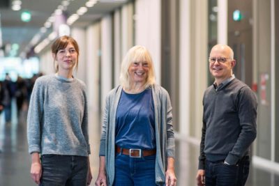 Drei Personen stehen lächeln in einem Flur.