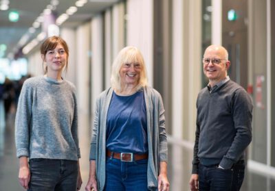 Drei Personen stehen lächeln in einem Flur.