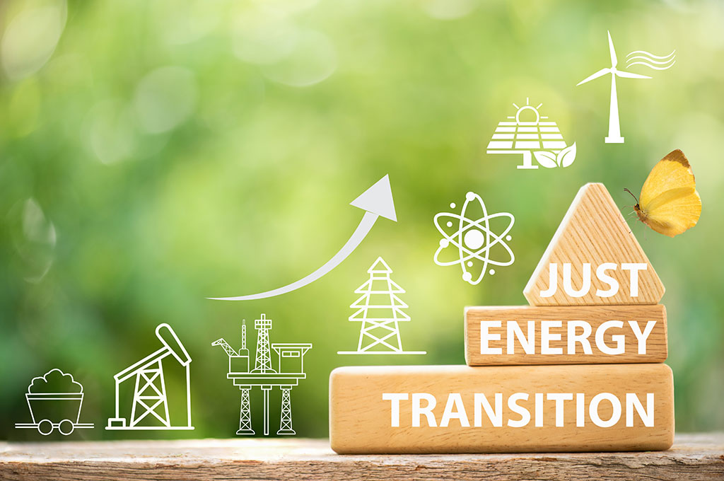 AdobeStock_1750886812 Drei gestlapelte Holzklötze mit der Aufschrift "Just Energy Transition" vor grünem Hintergrund. Links daneben der Verlauf der Energiewende dargstellt durch Grafikelemente der Energiegewinnungsarten im Verlauf der Zeit.
