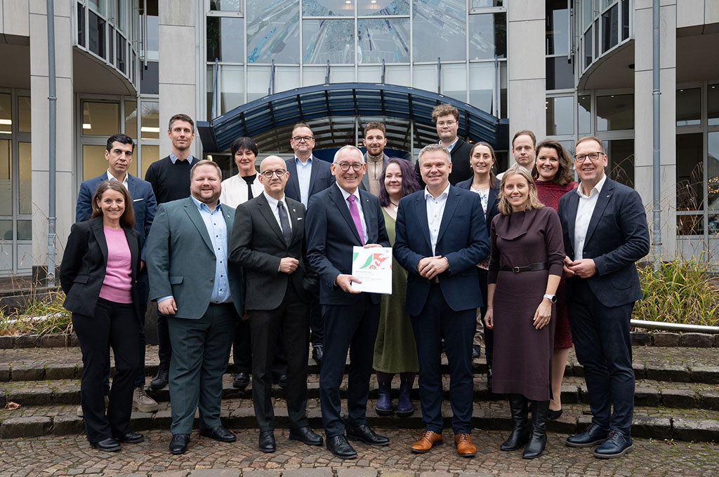 Eine Gruppe von Menschen steht auf eine Treppe vor dem Haupteingang eines Gebäudes mit einer großen Fensterfronten